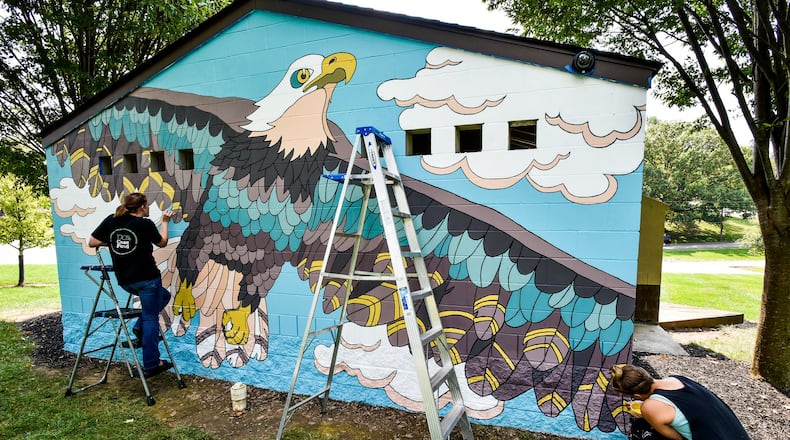 Melissa Smith (left) and Jenn Acus-Smith paint a mural on the restroom building at Veterans Park on New London Road in Hamilton. Acus-Smith designed murals for different locations in Hamilton parks. NICK GRAHAM/STAFF
