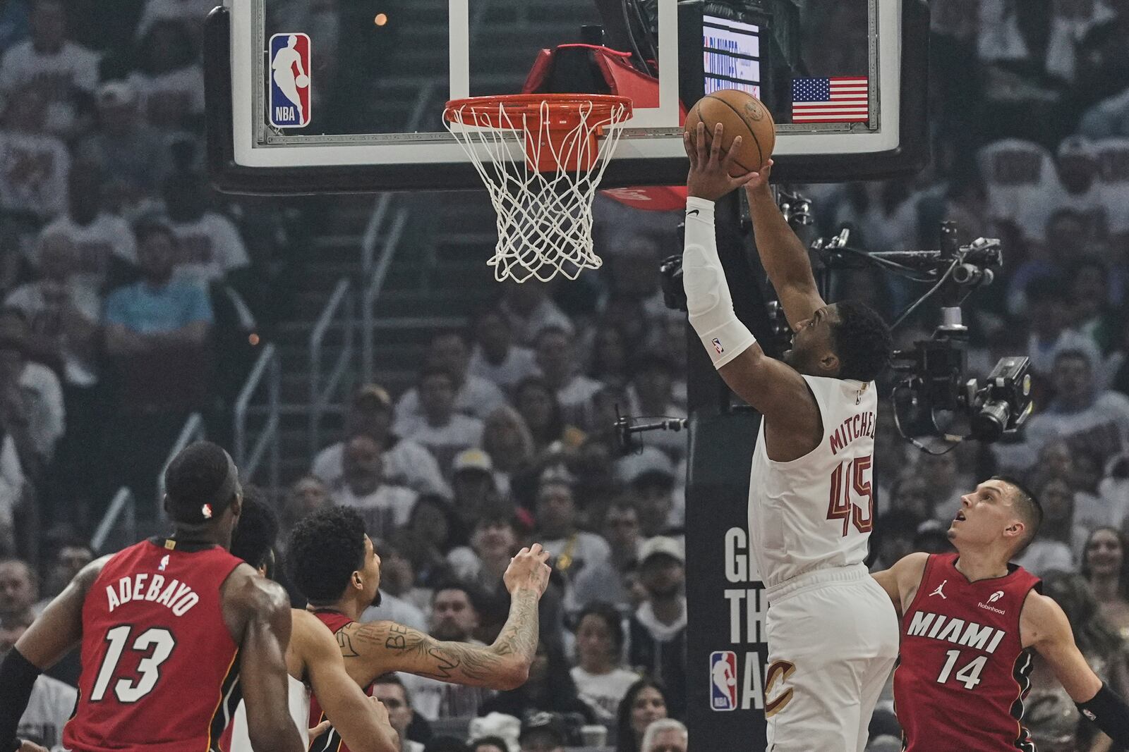 Cleveland Cavaliers guard Donovan Mitchell (45) goes up for a dunk between Miami Heat center Bam Adebayo (13) and guard Tyler Herro (14) in the first half in Game 1 of an NBA first-round playoff series, Sunday, April 20, 2025, in Cleveland. (AP Photo/Sue Ogrocki)