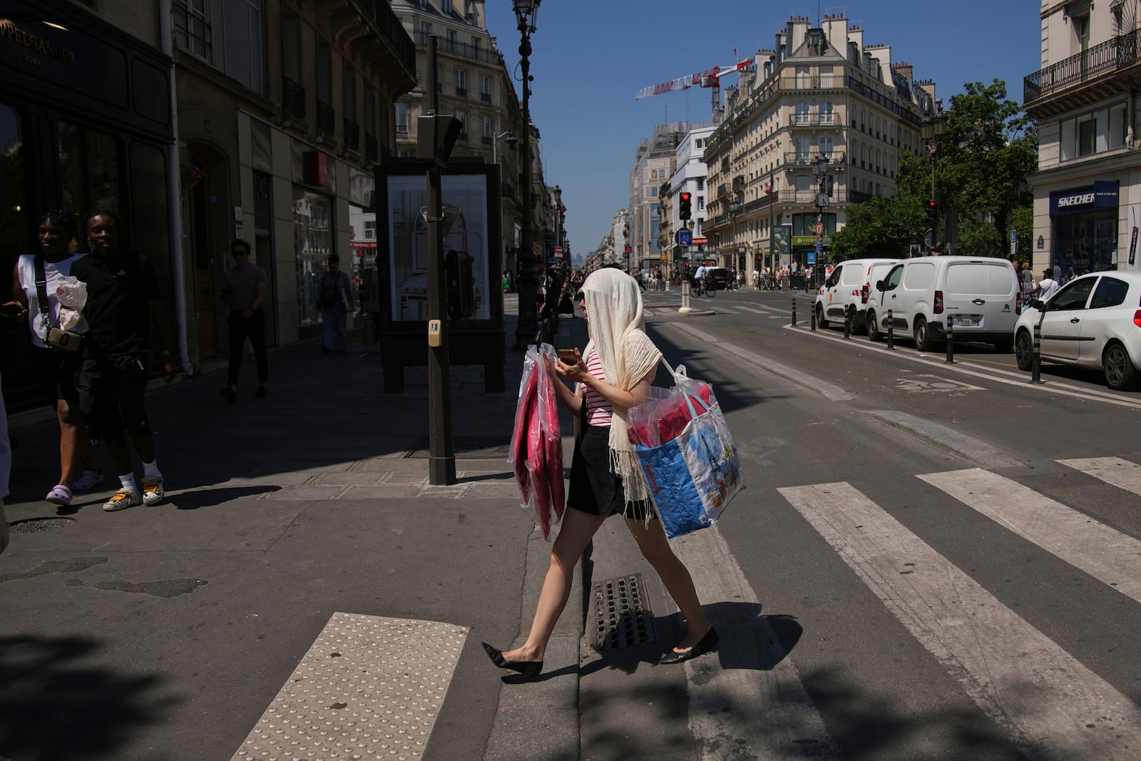 A woman protects her head during a heat wave, Monday, June 30, 2025 in Paris. (AP Photo/Christophe Ena)