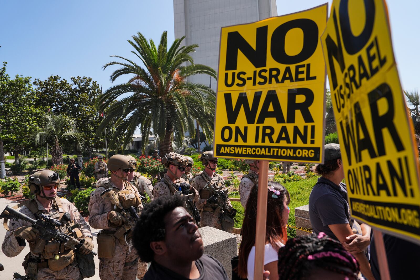 Anti-war demonstrators hold up signs as U.S. Marines guard the Wilshire Federal Building in Los Angeles, Sunday, June 22, 2025. (AP Photo/Jae C. Hong)