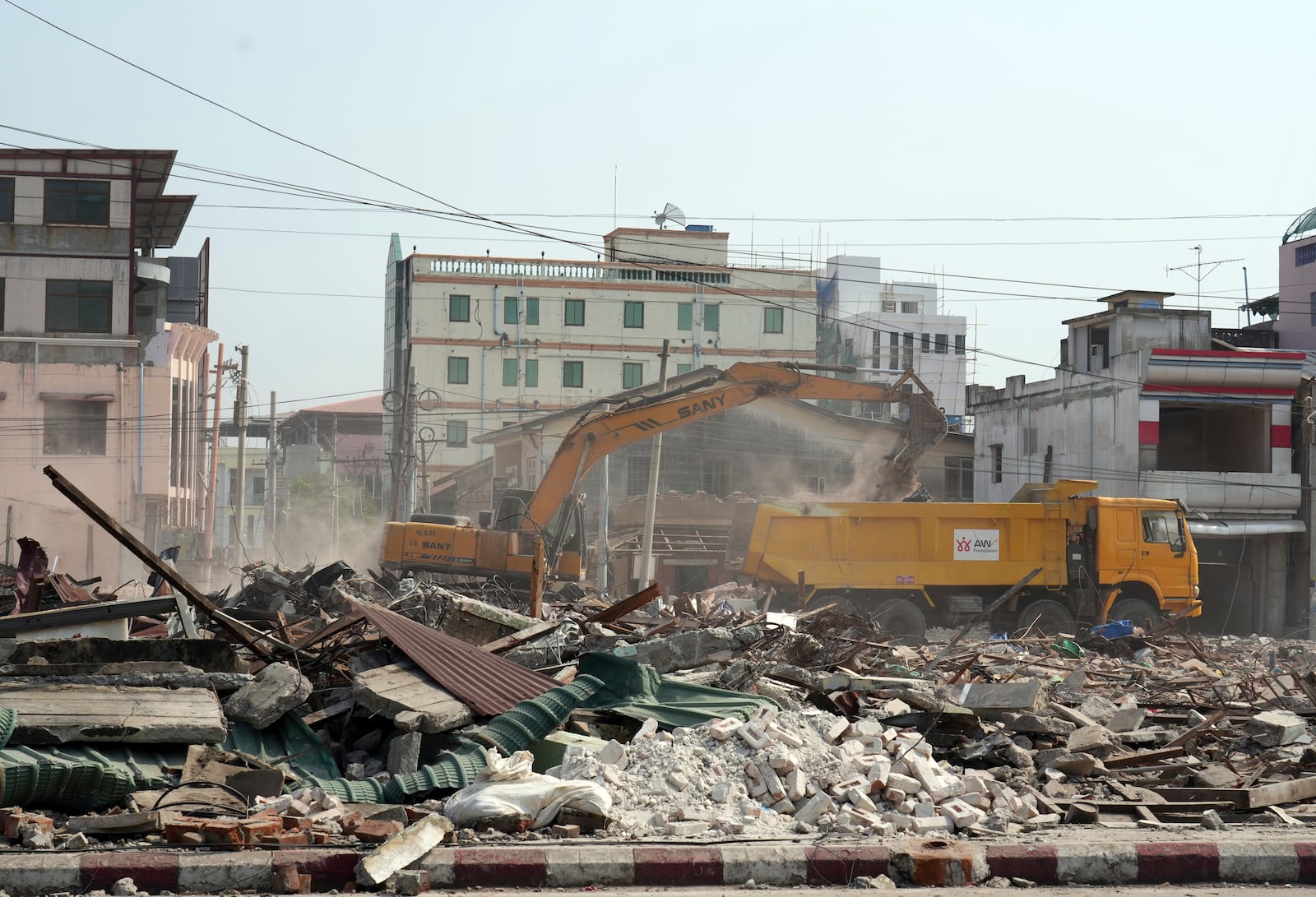 A volunteer drives a backhoe to clear debris of a building at a market, after one month of the strong earthquake in Naypyitaw, Myanmar, Monday, April 28, 2025. (AP Photo/Aung Shine Oo)
