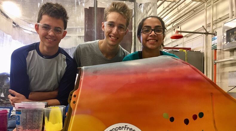 Three Butler Tech students — (from left) Daniel Walter, Andrew Johnson and Emely Giraldi — are putting the finishing touches on a child-sized pedal car they built to serve as an auction item next month to benefit CancerFree Kids. MICHAEL D. CLARK/STAFF