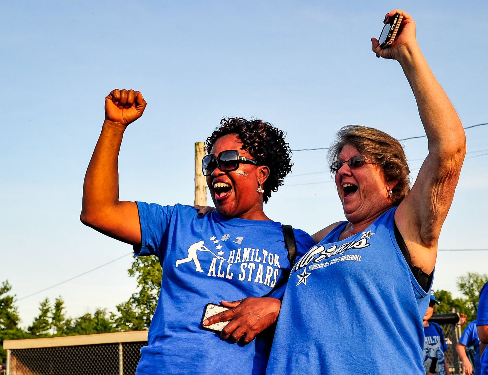 Fans Barbara Hirsch (left) and Susie Avery-Combs cheer for their Hamilton West Side Little League team after a 10-0 win over Lebanon on Monday in the District 9 tournament final at West Side. NICK GRAHAM/STAFF