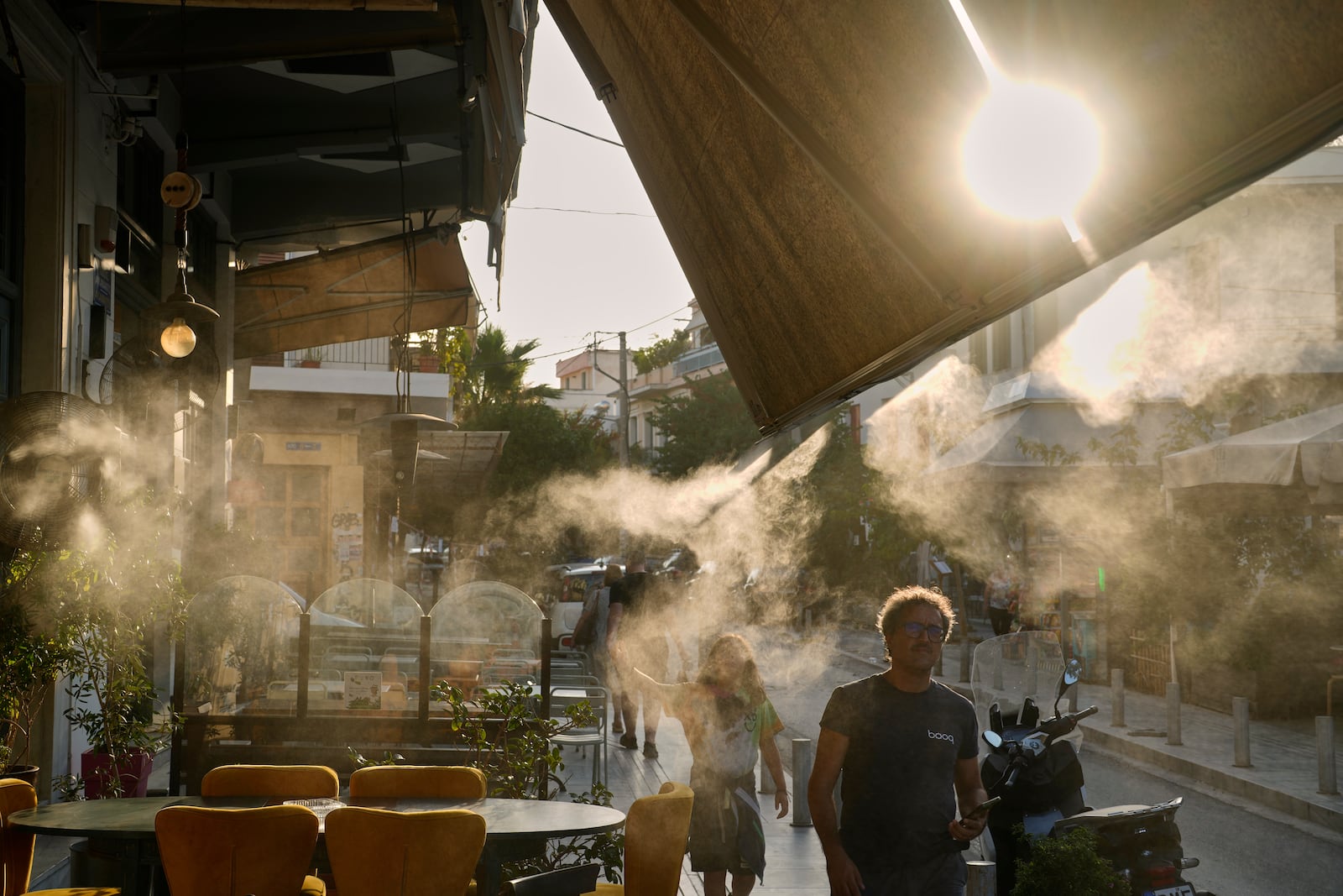 Pedestrians walk next to a mist machine in Thisio district of Athens during a heatwave, Tuesday, July 22, 2025.(AP Photo/Petros Giannakouris)