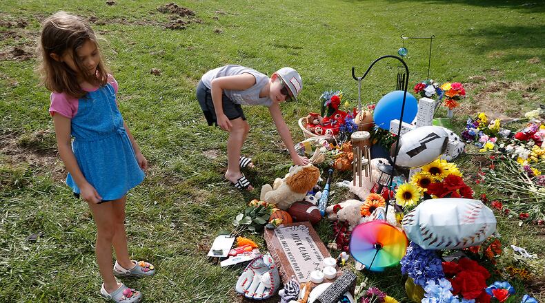 Leslie Walker and her step brother, Braxton Le Blanc, place their own stuffed animals at the fatal bus crash memorial along Troy Road Thursday, August 24, 2023. Both Leslie and Braxton were passengers on the bus when it crashed on Tuesday. This was the first time the children had returned to the site of the crash. BILL LACKEY/STAFF