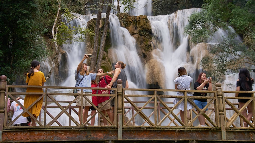 Tourists pose for photos on a footbridge in front of Kuang Si Waterfall near Luang Prabang, Laos, one of the country's most popular natural attractions known for its multi-tiered limestone cascades and turquoise pools on Tuesday, Nov. 4, 2025. (AP Photo/Eugene Hoshiko)
