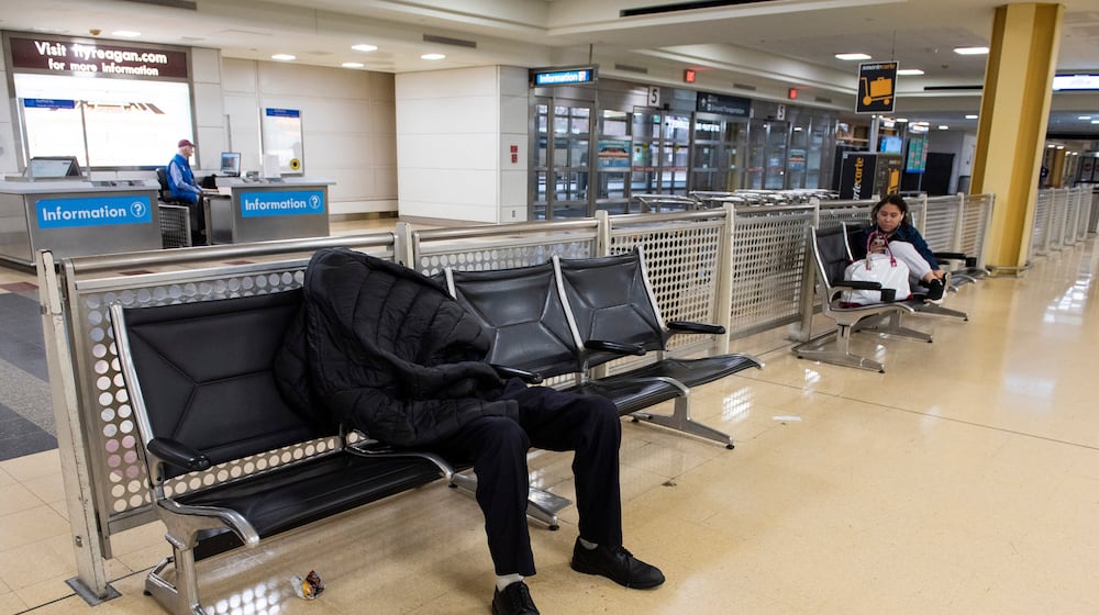 A man sleeps in the baggage claim area of Ronald Reagan National Airport, in Arlington, Va., Monday, March 16, 2026. (AP Photo/Cliff Owen)