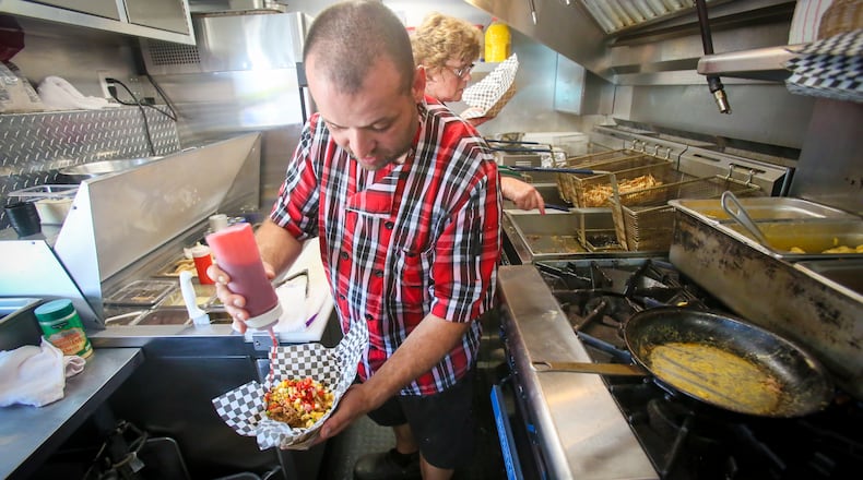 Vitor Abrue of the Urban Bistro food truck puts the finishing touches on a Pork'n'Cheese during the  Union Centre Food Truck Rally, Aug. 11, in West Chester Twp. GREG LYNCH / STAFF