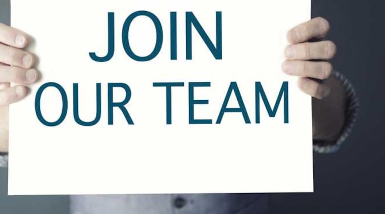 A man holds a sign that says now hiring.