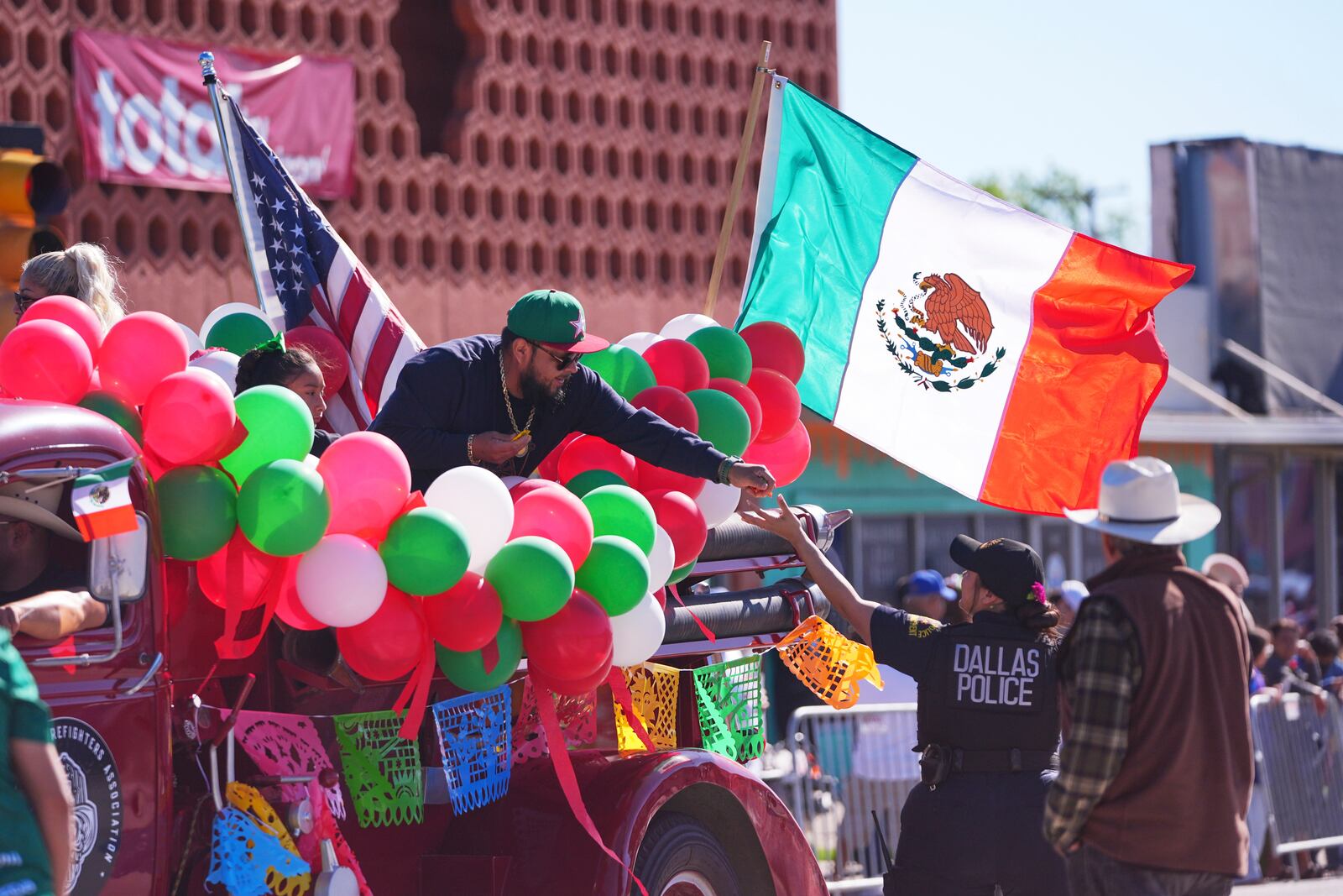 A float rider hands candy to a Dallas police officer during a Cinco de Mayo parade in the Oak Cliff section of Dallas, Saturday, May 3, 2025. (AP Photo/LM Otero)