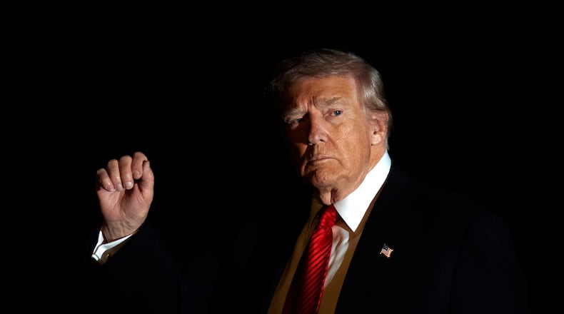 President Donald Trump is illuminated by a camera flash as he gestures while walking across the South Lawn of the White House, Sunday, Nov. 2, 2025, in Washington, after returning from a trip to Florida. (AP Photo/Mark Schiefelbein)
