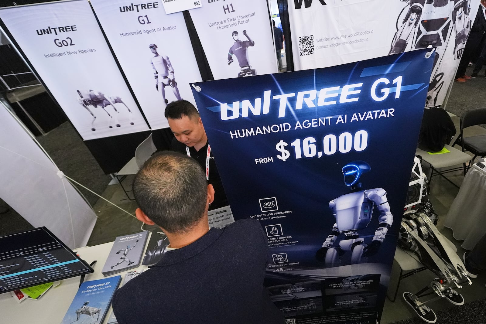 Unitree company representative talks with a convention guest at the company's product booth at the Robotics Summit & Expo, Wednesday, April 30, 2025, in Boston. (AP Photo/Charles Krupa)