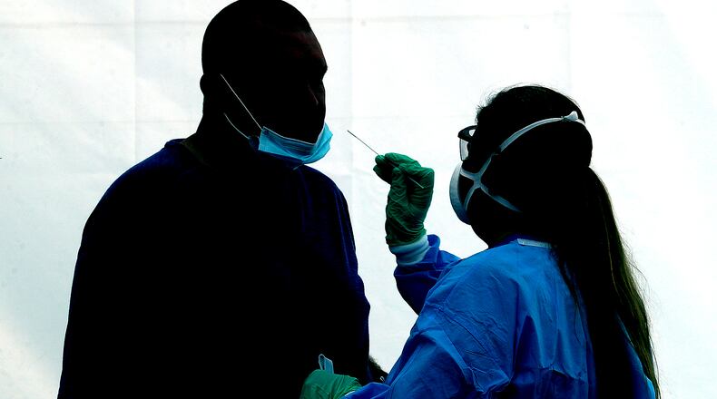 A man is silhouetted against the wall of a white tent as he gets a COVID-19 test at the Clark County Combined Health District's free COVID testing clinic at Hayward Middle School. BILL LACKEY/STAFF