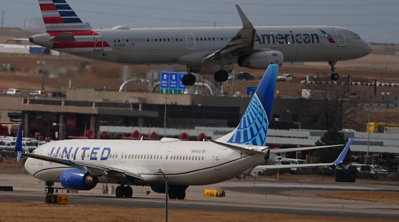 An American Airlines jetliner lands on a runway as a United Airlines plane waits for clearance to take off as high winds strafe Denver International Airport Thursday, March 12, 2026, in Denver. (AP Photo/David Zalubowski)