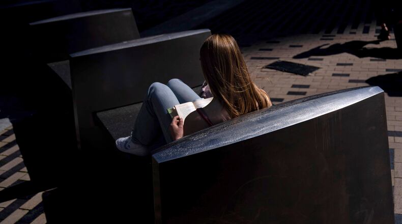 FILE - A woman reads a book in the afternoon sun on a bench outside South Station in Boston, on Friday, May 31, 2024. (AP Photo/David Goldman, File)