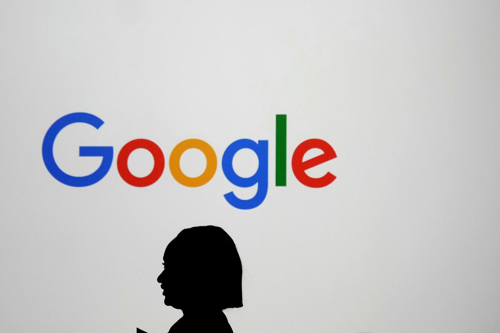 FILE - A woman walks by a giant screen with a logo at an event at the Paris Google Lab on the sidelines of the AI Action Summit in Paris, Sunday, Feb. 9, 2025. (AP Photo/Thibault Camus, File)