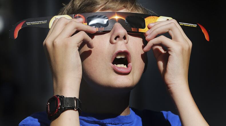 In this Wednesday, Aug. 16,photo, Colton Hammer tries out his new eclipse glasses he just bought from the Clark Planetarium in Salt Lake City in preparation for the eclipse. (Scott G Winterton/The Deseret News via AP)