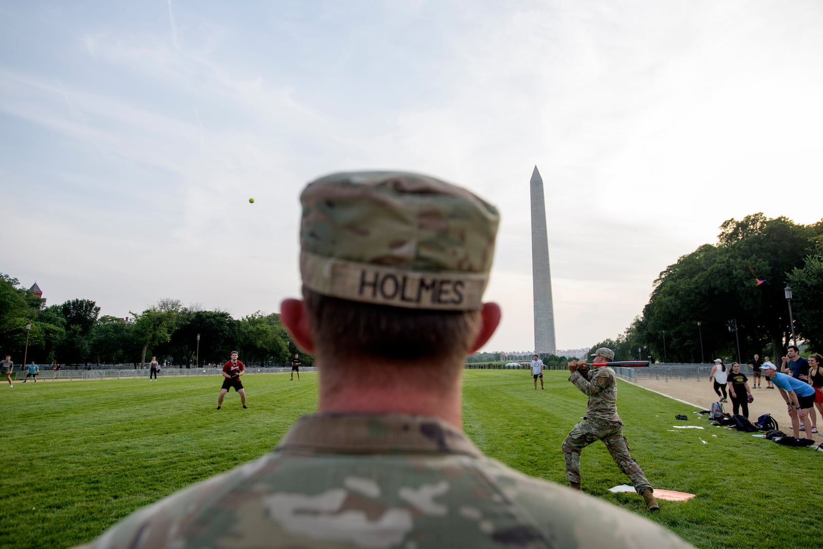 Seen through security fencing, Army Spc. Steven Holmes, left, watches Army Sgt. Chase Beasley, right, take a swing as they sit-in on a game of softball with congressional staffers on the National Mall, during preparations for an upcoming military parade commemorating the Army's 250th anniversary and coinciding with President Donald Trump's 79th birthday, Thursday, June 12, 2025, in Washington. (AP Photo/Rod Lamkey, Jr.)