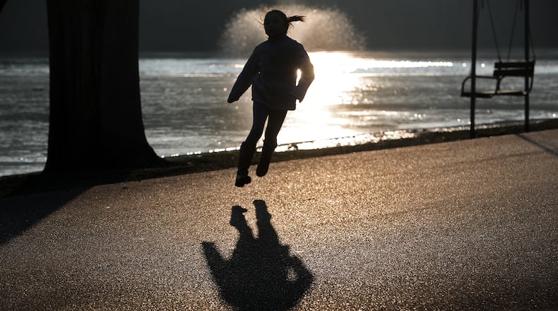 A young girl is silhouetted in the evening sun as she skips along the roadway in Snyder Park Tuesday to catch up to her father. BILL LACKEY/STAFF