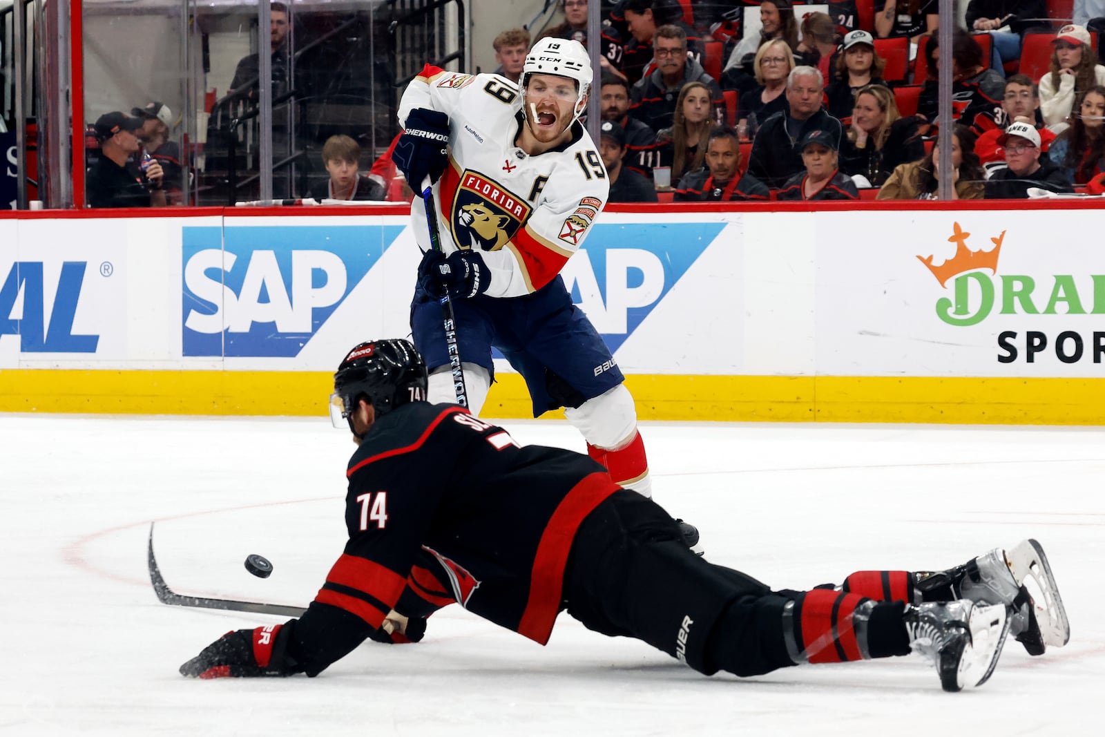 Florida Panthers' Matthew Tkachuk (19) passes the puck around a sliding Carolina Hurricanes' Jaccob Slavin (74) during the third period of Game 2 of the NHL hockey Stanley Cup Eastern Conference finals in Raleigh, N.C., Thursday, May 22, 2025. (AP Photo/Karl DeBlaker)