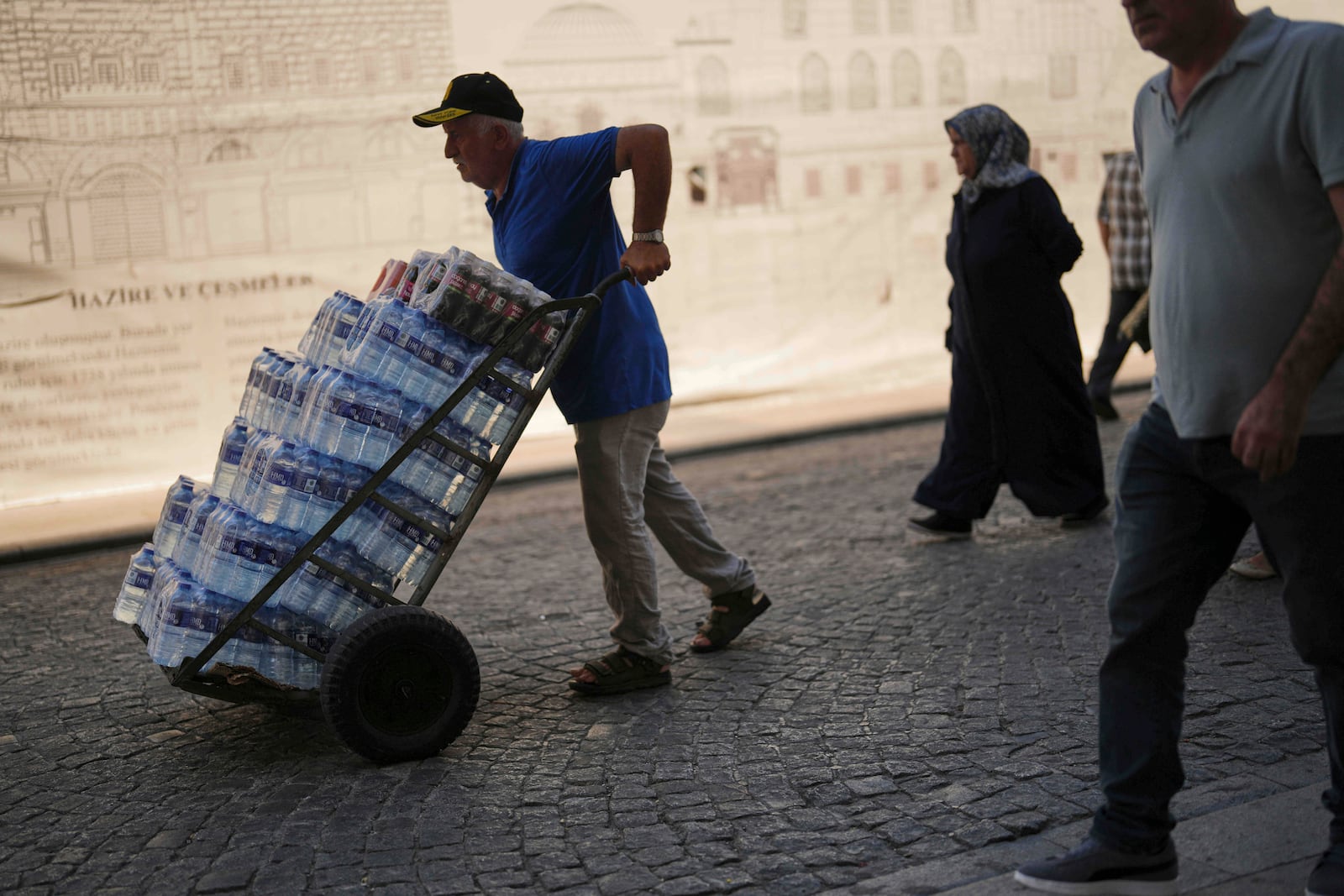 A man delivers plastic bottles of water to a local restaurant on a hot summer day at Eminonu district, in Istanbul, Turkey, Friday, July 25, 2025. (AP Photo/Francisco Seco)