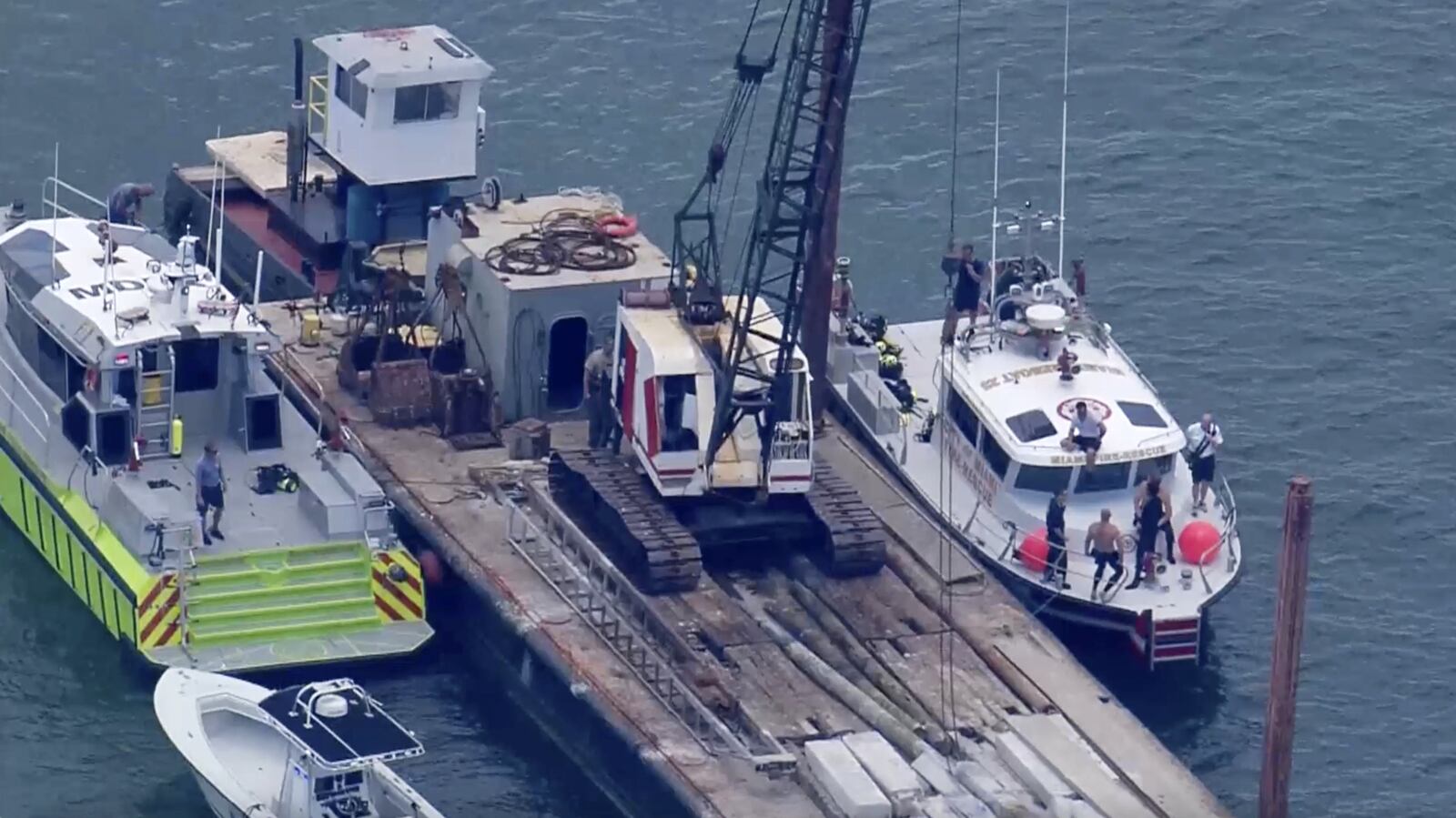 This image taken from video provided by WSVN-TV shows Miami-Dade Fire Rescue and others in boats around what appears to be a barge involved in an accident with a group of kids and an adult on a sailing boat during a sailing camp, Monday, July 28, 2025, in Miami. (WSVN-TV via AP)