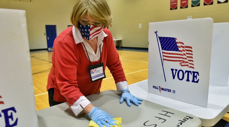 Poll worker Patty Mays cleans a table between voters on election day at the polling location at Wilson Middle School Tuesday, Nov. 3, 2020 in Hamilton. NICK GRAHAM / STAFF