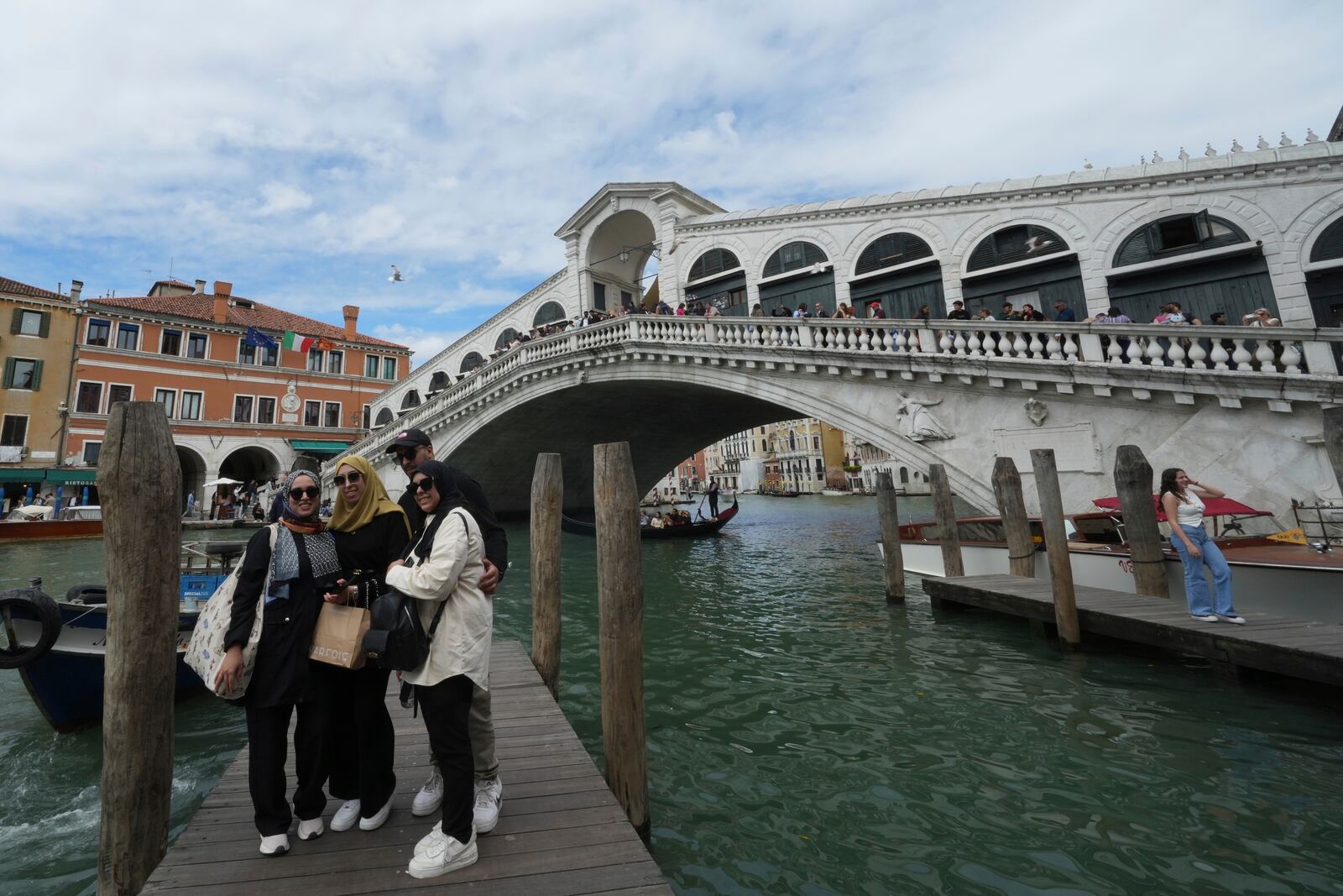 Tourists take pictures next Rialto Bridge "Ponte di Rialto" in Venice, Italy, Friday, April 18, 2025, Venice on Friday launches for a second year a pilot program to charge day-trippers an entrance fee. (AP Photo/Antonio Calanni)