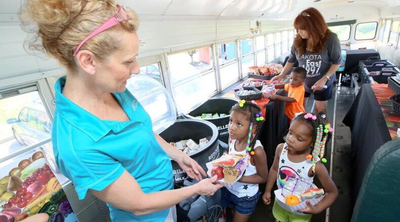 In this 2016 file photo, Lakota Schools Nutrition Manager Peggy Phebus and bus driver Melinda Robers talk with Kynnedi, Kaliya, and Elijah Staples as they pick out their lunch on board the Lakota Schools food bus during a stop at Meadow Ridge apartments during the mobile lunch program. GREG LYNCH / STAFF