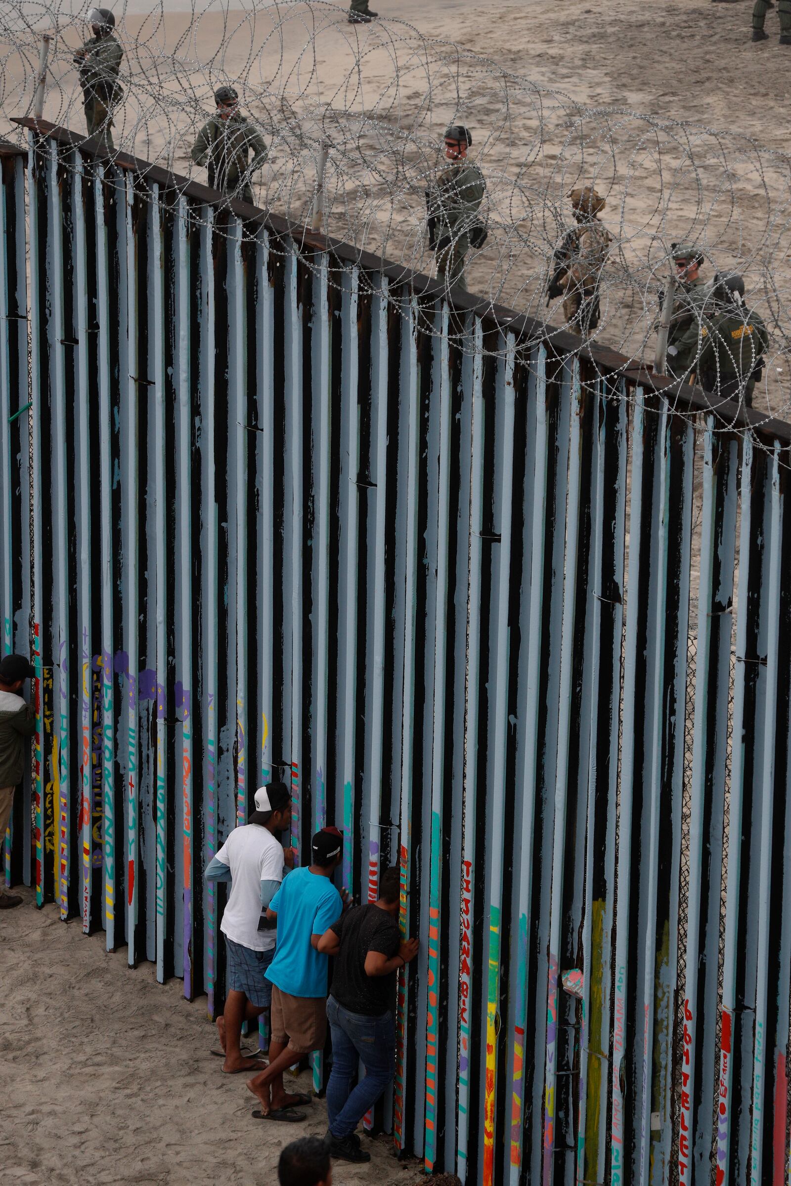 FILE - Young men peer through the border wall as U.S. Border Patrol in San Diego prepare for the arrival of hundreds of pro-migration protesters, in Tijuana, Mexico, Dec. 10, 2018. (AP Photo/Rebecca Blackwell, File)