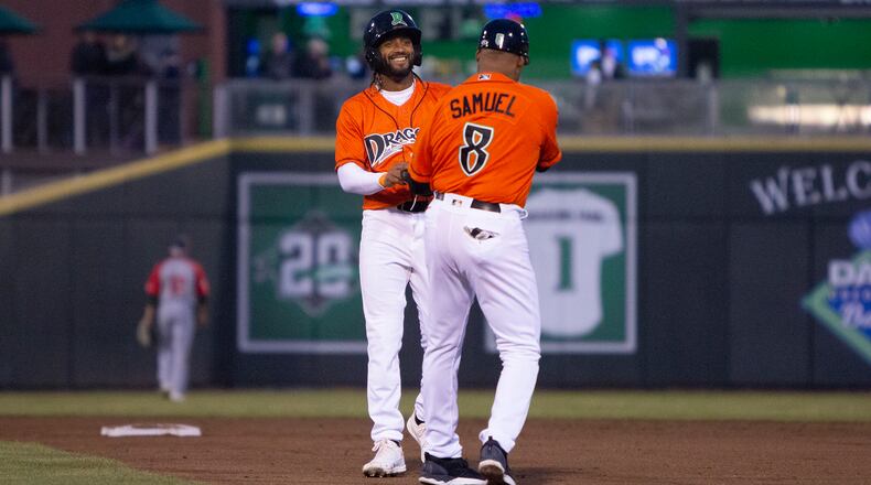 Dayton second baseman Jose Torres gives his batting gear to first-base coach Juan Samuel after hitting an RBI double during the season opener at DayAir Ballpark. Jeff Gilbert/CONTRIBUTED
