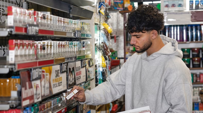 Store associate Ahmad Hamdan stocks Basic cigarettes as he starts his shift at the Eastown Smoke Shop on Monday, Dec. 15, 2025, in Dayton. JOSEPH COOKE/STAFF