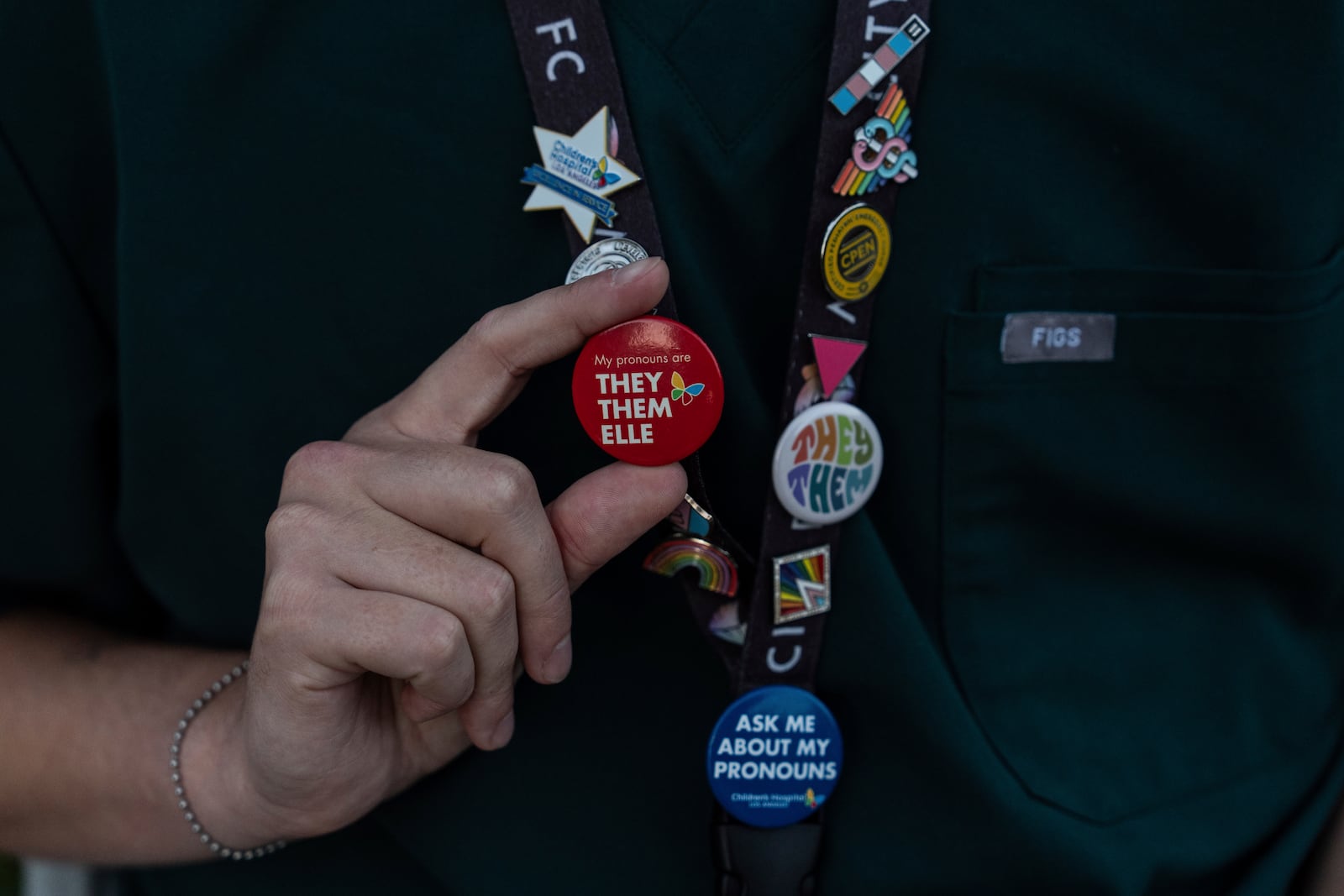 Jack Brenner, left, an emergency room nurse at Children's Hospital Los Angeles, shows a lanyard decorated with pronoun pins and buttons during a protest against the closure of the hospital's trans youth clinic Thursday, July 3, 2025, in Los Angeles. (AP Photo/Jae C. Hong)