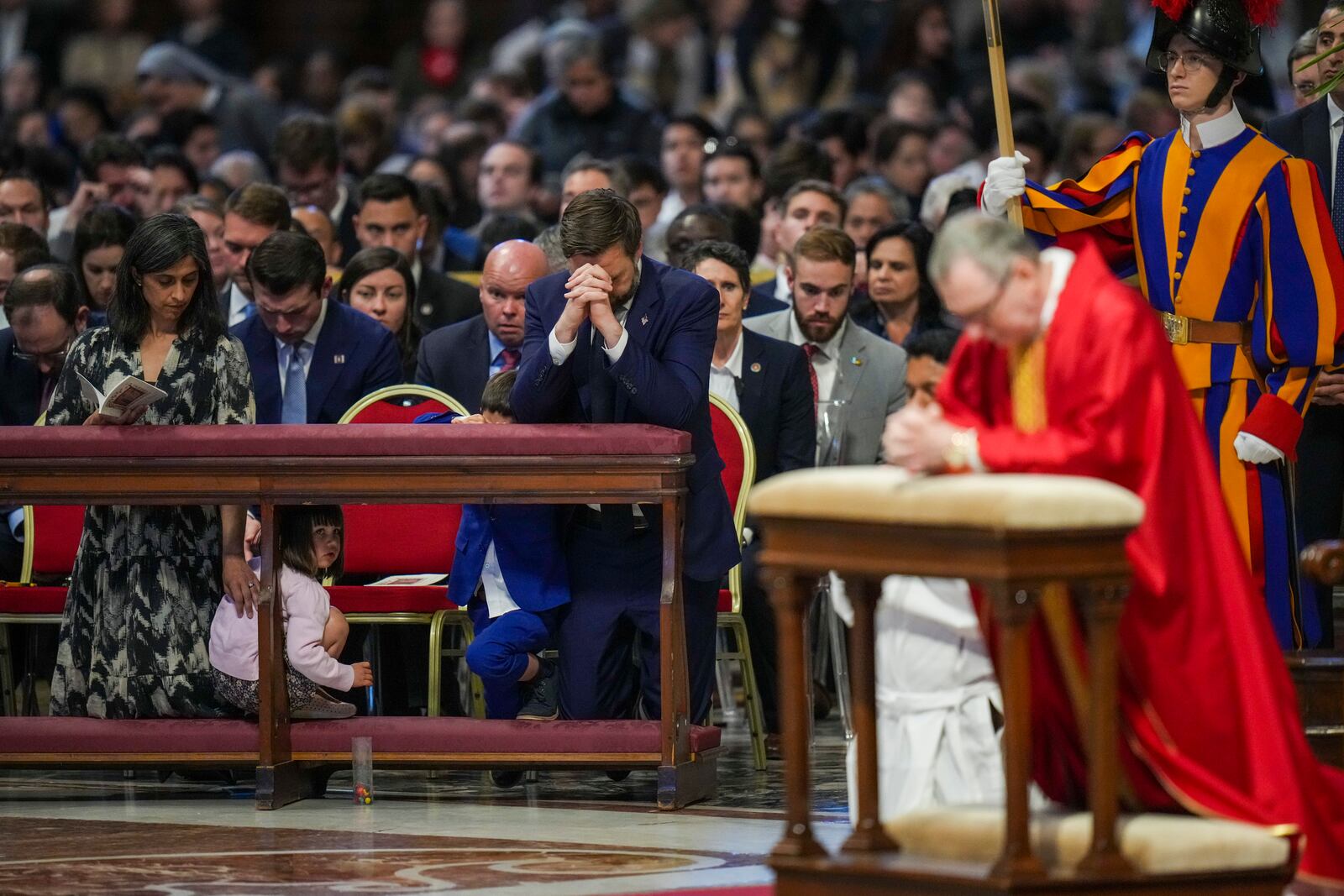 U.S. Vice President JD Vance, and his wife Usha Vance, left, with their daughter Mirabel attend a Good Friday service led by Cardinal Claudio Gugerotti, right, inside St. Peter's Basilica at the Vatican, Friday, April 18, 2025. (AP Photo/Alessandra Tarantino)