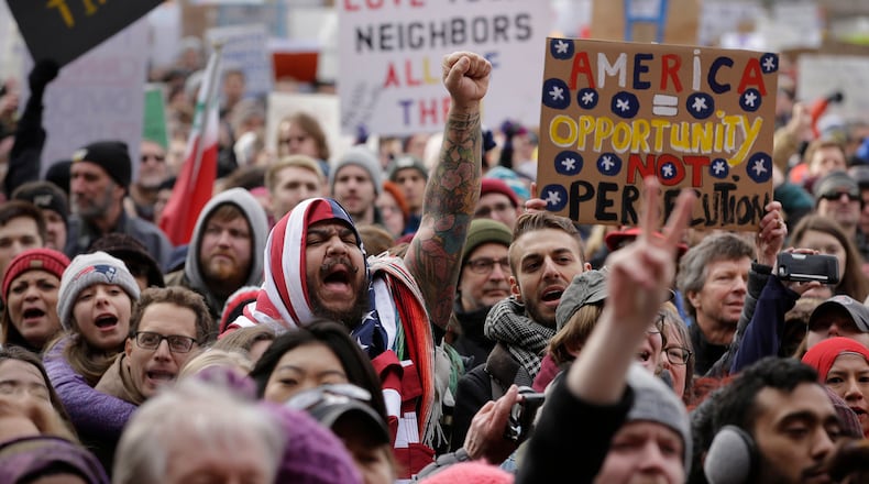 Izzy Berdan, of Boston, center, wears an American flags as he raises his arm and chants slogans with other demonstrators during a rally against President Trump's order that restricts travel to the U.S., Sunday, Jan. 29, 2017, in Boston. On Thursday, Feb. 16, 2017, immigrants across the nation will take part in "A Day Without Immigrants," a protest meant to show how immigrant dollars impact the U.S. economy. (AP Photo/Steven Senne)