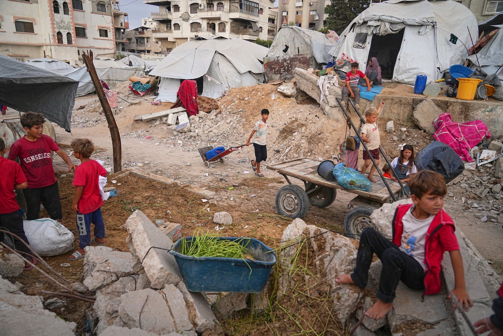 Palestinian youth and children are seen at a tent camp set up amid war-damaged infrastructure in Gaza City, Monday, June 23, 2025. (AP Photo/Jehad Alshrafi)