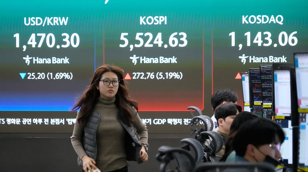 A currency trader passes by a screen showing the Korea Composite Stock Price Index (KOSPI), rear center, and the foreign exchange rate between U.S. dollar and South Korean won, rear left, at the foreign exchange dealing room of the Hana Bank headquarters in Seoul, South Korea, Tuesday, March 10, 2026. (AP Photo/Ahn Young-joon)