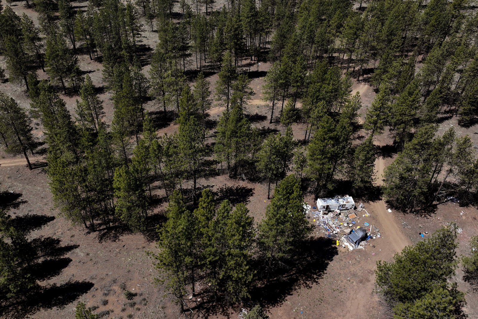 Debris lies scattered around a trailer at a homeless encampment in Deschutes National Forest, Thursday, May 1, 2025, near Bend, Ore. (AP Photo/Jenny Kane)