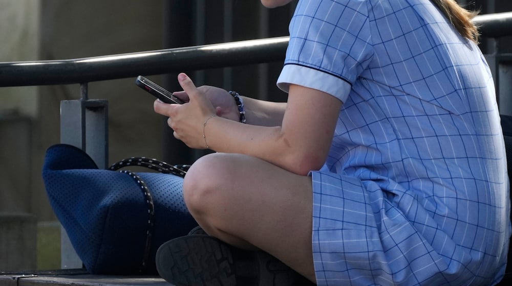 FILE - A young girl uses her phone while sitting on a bench in Sydney, Nov. 8, 2024. (AP Photo/Rick Rycroft, File)