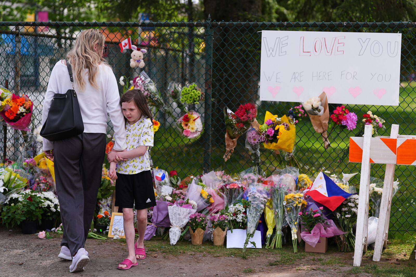 Visitors stand near a growing memorial the day after a driver killed multiple people during a Filipino community festival Sunday, April 27, 2025, in Vancouver, British Columbia. (AP Photo/Lindsey Wasson)