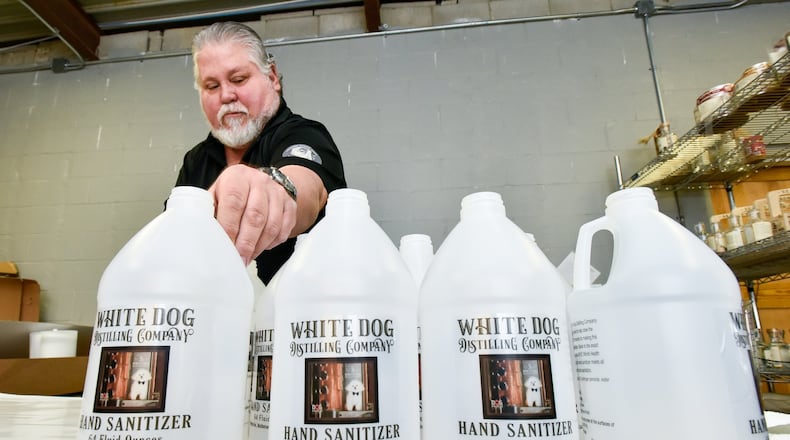 Mike Dranschak puts labels on half gallon jugs that will be filled with hand sanitizer at his Central Avenue business, White Dog Distilling Company, Monday, March 30, 2020 in Middletown. Dranschak has switched from making his usual vodka, rum, gin and agave spirits to producing hand sanitizer during the coronavirus (COVID-19) pandemic. The line in front of his business has extended down the street every day since they started selling the sanitizer. NICK GRAHAM / STAFF