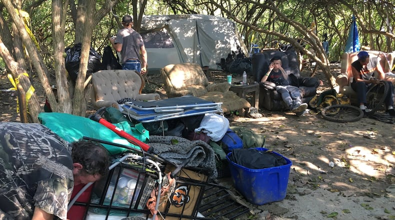 John Thomas, left, makes adjustments Sunday to a cart he planned to pull behind a bicycle to remove his possessions from a homeless tent camp behind Hamilton Plaza. MIKE RUTLEDGE/STAFF
