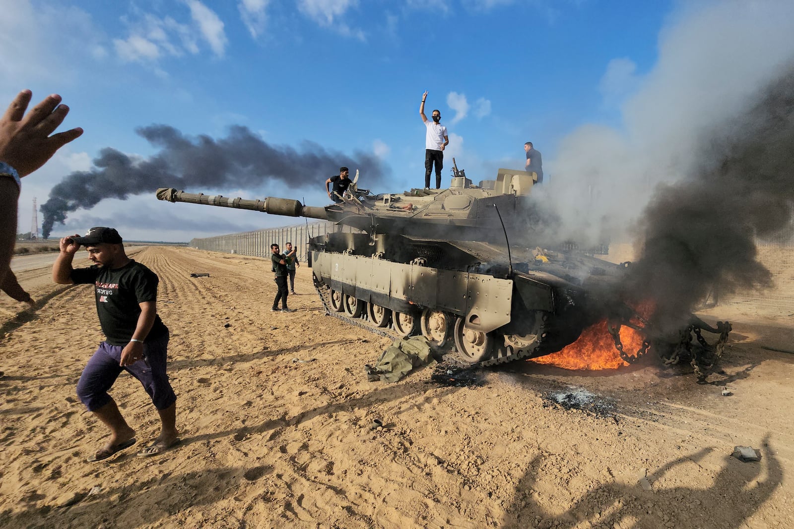 FILE - Palestinians celebrate by a destroyed Israeli tank at the border fence between Israel and the Gaza Strip, east of Khan Younis, during a surprise attack on Israel, Saturday, Oct. 7, 2023. (AP Photo, File)