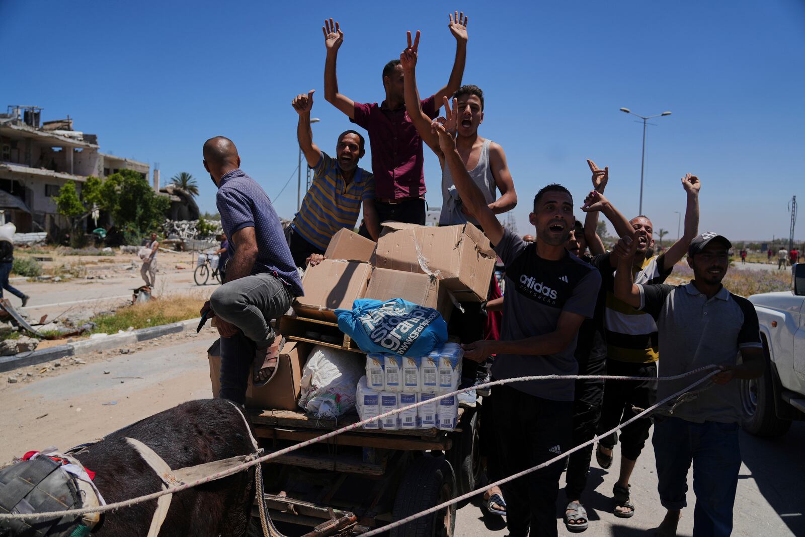 Palestinians wave to the camera as they carry boxes and bags containing food and humanitarian aid packages delivered by the Gaza Humanitarian Foundation, a U.S.-backed organization approved by Israel, in Khan Younis, southern Gaza Strip, on Thursday, May 29, 2025. (AP Photo/Abdel Kareem Hana)