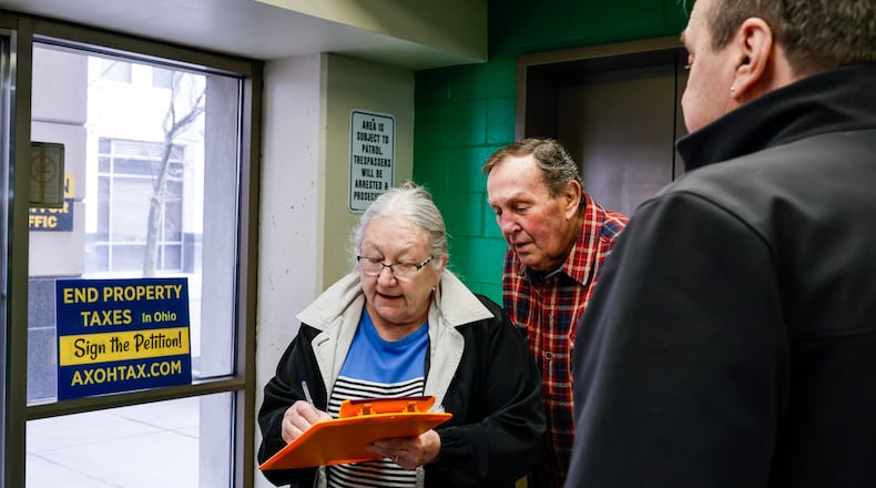 Jim Fescina, right, with AxOhioTax, gets signatures from Rob and Belinda Batdorf as they go in to pay taxes Thursday, Feb. 26, 2026 at Butler County Government Services Center building on High Street in Hamilton. AxOhioTax was collecting signatures in order to put property tax repeal on the November ballot. NICK GRAHAM/STAFF