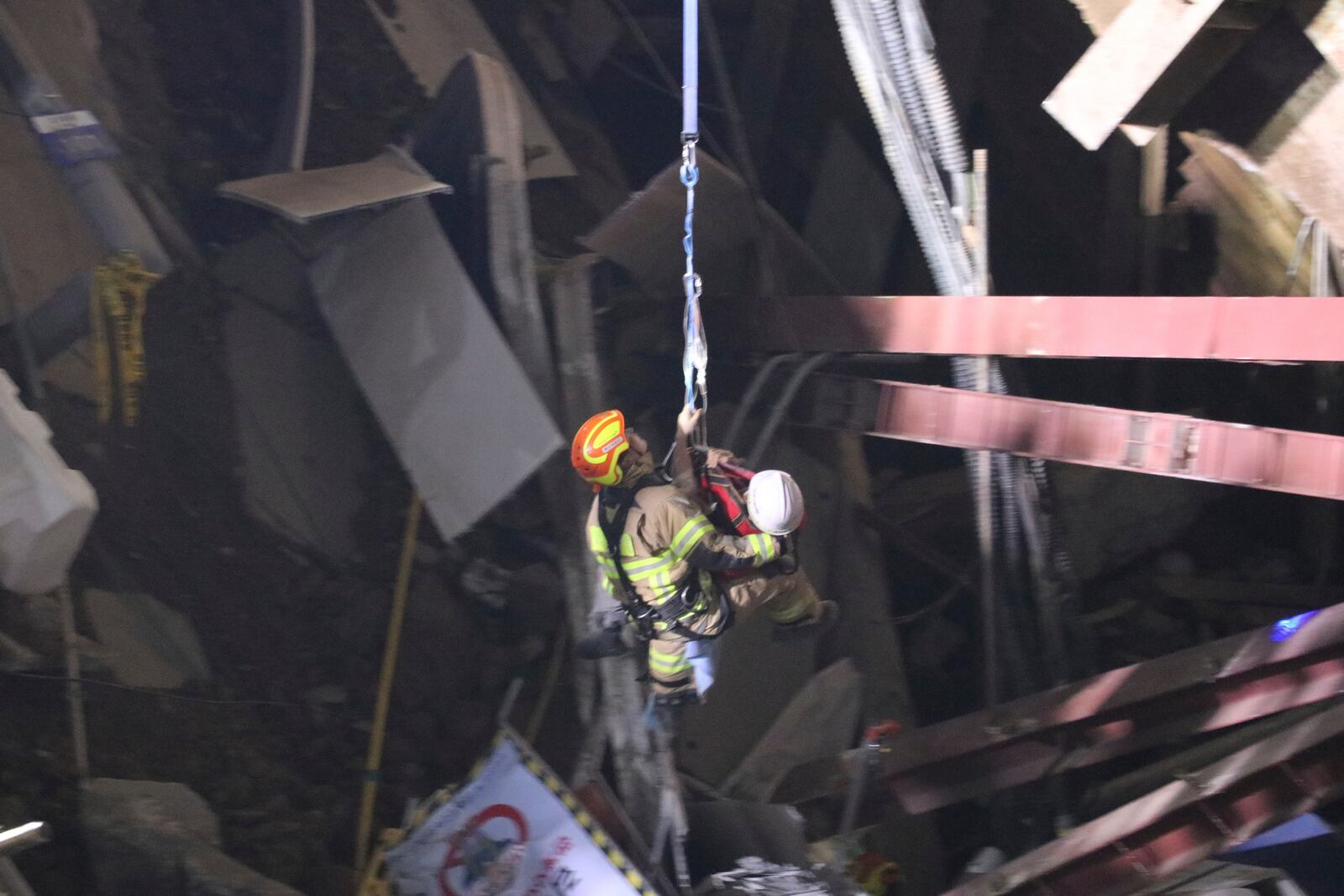 In this photo provided by South Korea Gyeonggi-do Fire Services, a survivor wearing white helmet, is rescued by a firefighter at the scene of a collapsed subway construction site in Gwangmyeong, South Korea, Saturday, April 12, 2025. (South Korea Gyeonggi-do Fire Services via AP)
