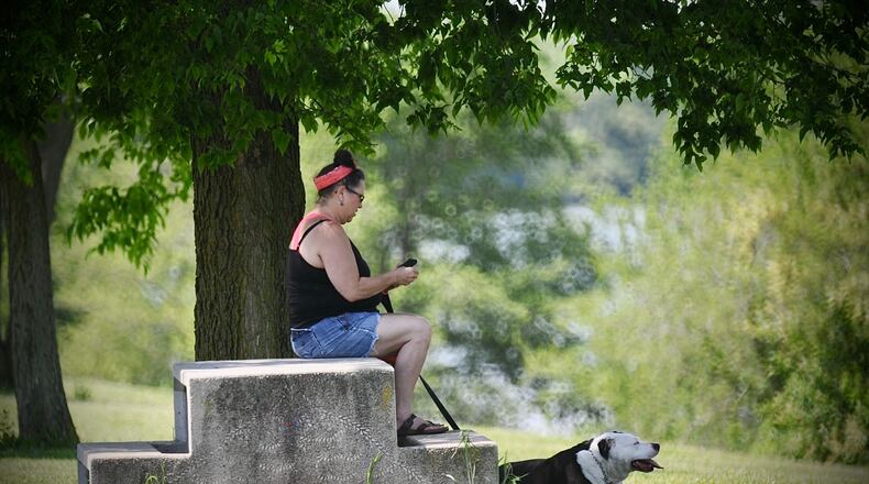 A woman and her dog take a break under a the shade of a tree May 21, 2021, after walking around Eastwood Lake Park in Dayton. MARSHALL GORBY\STAFF