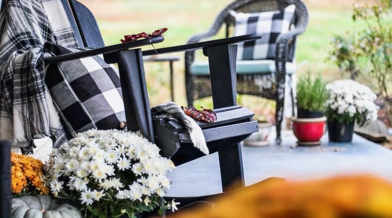 Fall is a time to cozy up your outdoor living space. Adding an Adirondack rocking chair with a traditional style buffalo check blanket and pillows on a porch or patio decorated for autumn with heirloom gourds and mums is one idea. ISTOCK