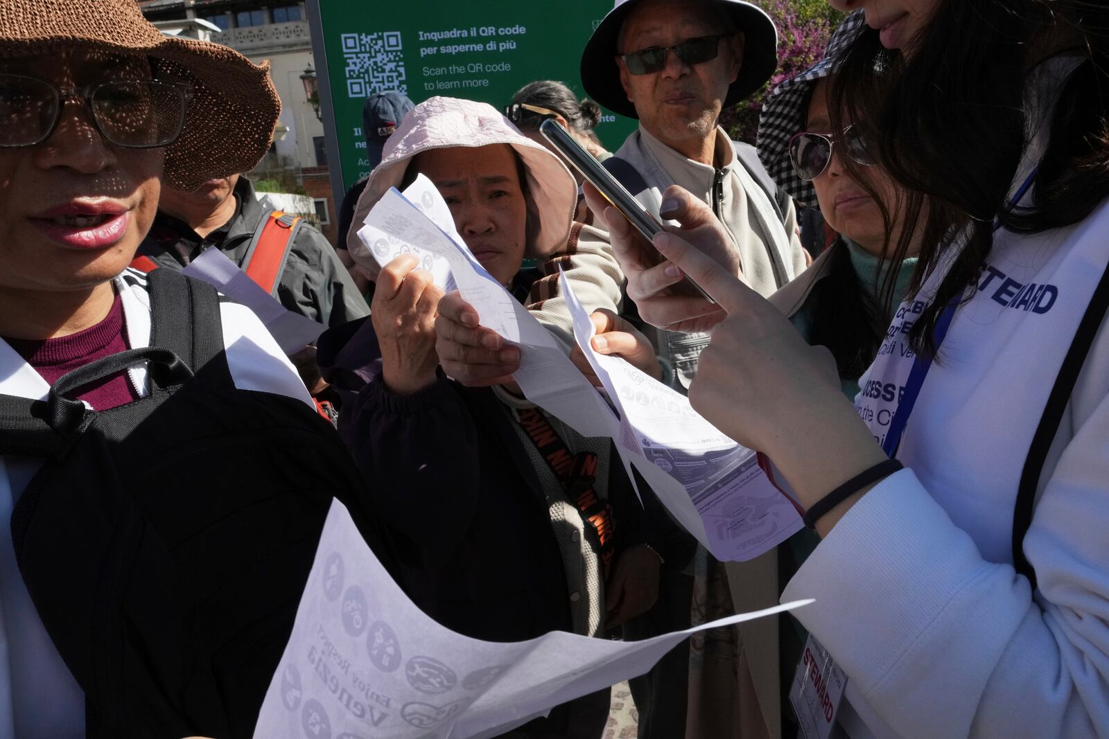 Stewards check tourists' QR codes outside the main train station in Venice, Italy, Friday, April 18, 2025, as the city for a second year is charging day-trippers an arrivals tax. (AP Photo/Antonio Calanni)