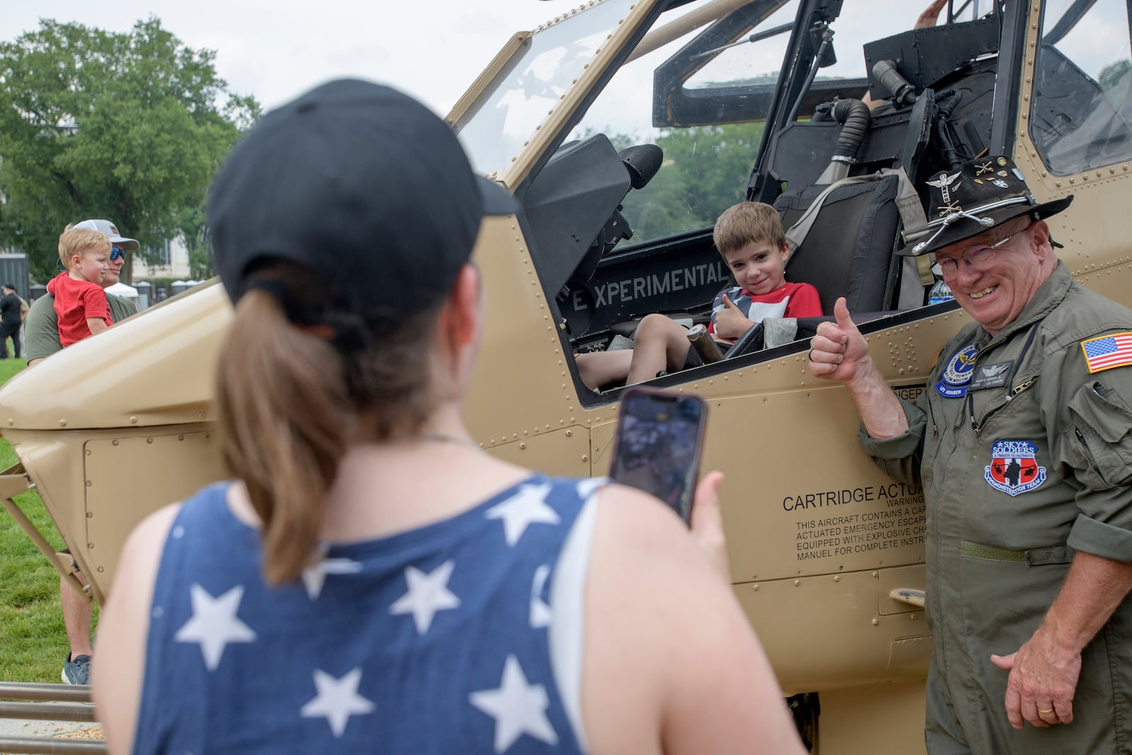 Retired Army CW4 Floyd Werner Jr., right, poses with Victor Koza, 5, center, as his mother, Melinda Koza, left, takes a photo in front of an AH-1F Cobra 998 helicopter during an event to honor the Army's 250th anniversary, coinciding with President Donald Trump's 79th birthday, Saturday, June 14, 2025, in Washington. (AP Photo/Rod Lamkey, Jr.)